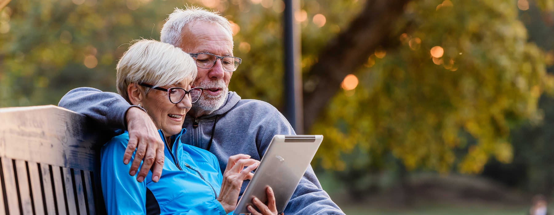 elderly couple look at their e-pad on park bench
